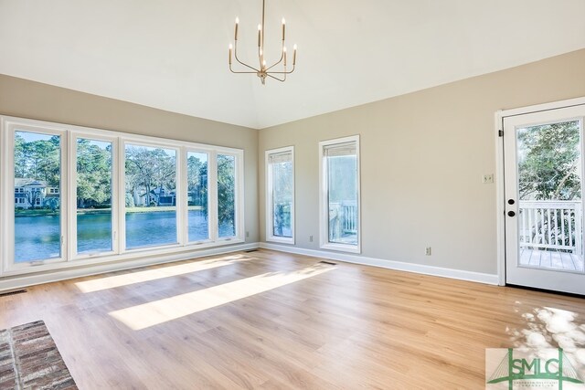 interior space featuring light hardwood / wood-style flooring, a healthy amount of sunlight, vaulted ceiling, and an inviting chandelier