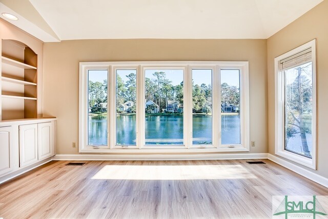 spare room featuring built in features, a water view, lofted ceiling, and light hardwood / wood-style flooring