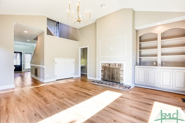 unfurnished living room with built in shelves, light wood-style flooring, an inviting chandelier, a brick fireplace, and high vaulted ceiling