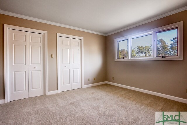 unfurnished bedroom with ornamental molding, light carpet, and two closets