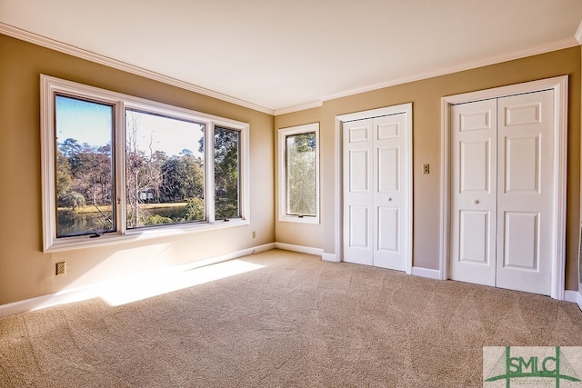 unfurnished bedroom featuring carpet, crown molding, baseboards, and two closets