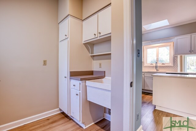 kitchen featuring decorative backsplash, a skylight, sink, light hardwood / wood-style flooring, and white cabinets