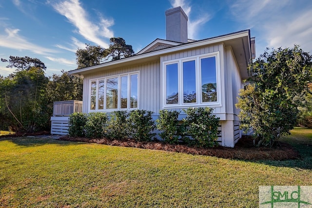 view of side of property featuring board and batten siding, a chimney, and a lawn