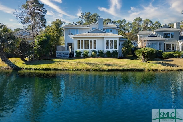 rear view of house with a water view, a lawn, and a chimney