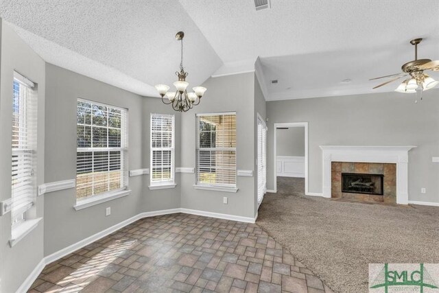 unfurnished dining area featuring a textured ceiling, ceiling fan with notable chandelier, lofted ceiling, and a fireplace