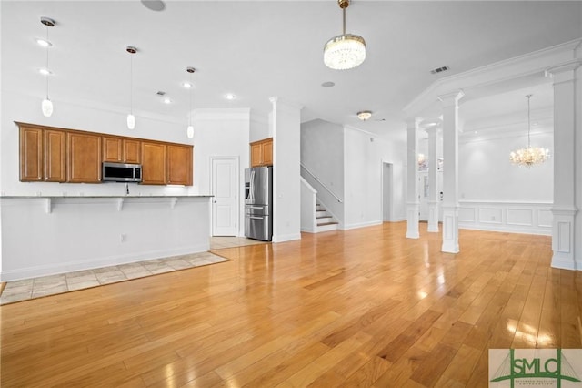 unfurnished living room with light hardwood / wood-style floors, an inviting chandelier, crown molding, and decorative columns