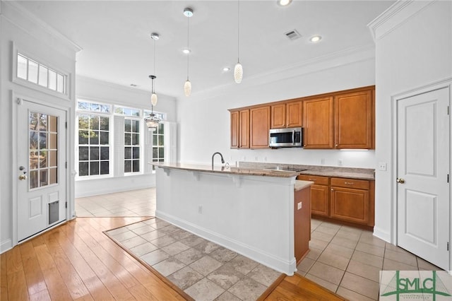 kitchen featuring light wood-type flooring, a center island with sink, hanging light fixtures, crown molding, and a kitchen breakfast bar