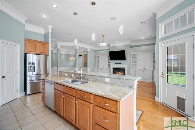 kitchen with sink, pendant lighting, crown molding, stainless steel appliances, and a kitchen island with sink