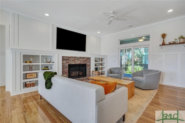 living room featuring crown molding, a brick fireplace, built in features, ceiling fan, and light hardwood / wood-style floors