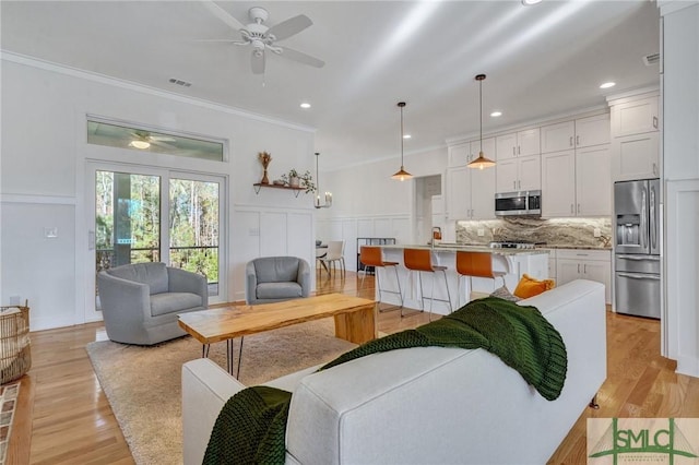 living room with ornamental molding, light hardwood / wood-style floors, and ceiling fan