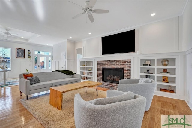 living room with built in shelves, crown molding, light wood-type flooring, ceiling fan, and a fireplace