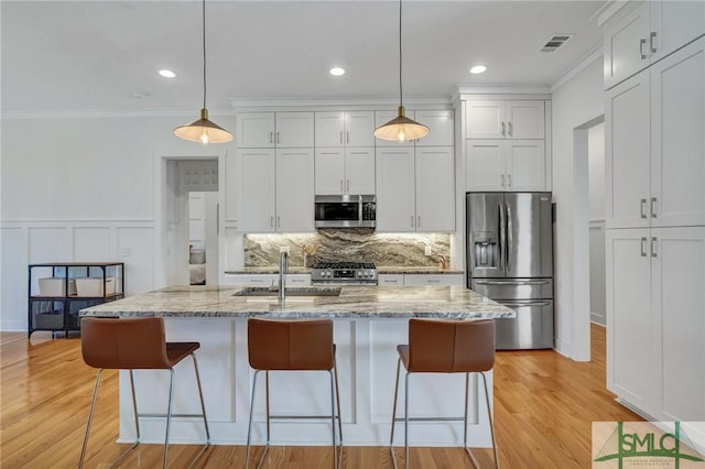 kitchen featuring sink, hanging light fixtures, stainless steel appliances, light stone counters, and an island with sink