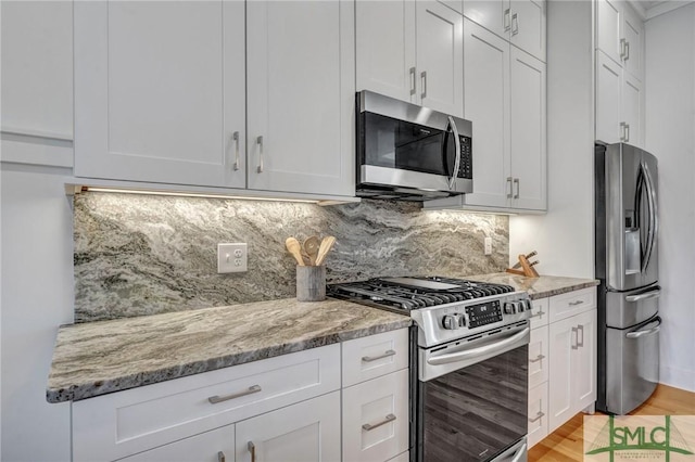 kitchen featuring light stone countertops, appliances with stainless steel finishes, white cabinets, and backsplash