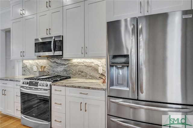 kitchen with light wood-type flooring, white cabinets, stainless steel appliances, light stone countertops, and backsplash