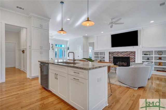 kitchen with light stone countertops, stainless steel dishwasher, a center island with sink, and white cabinets