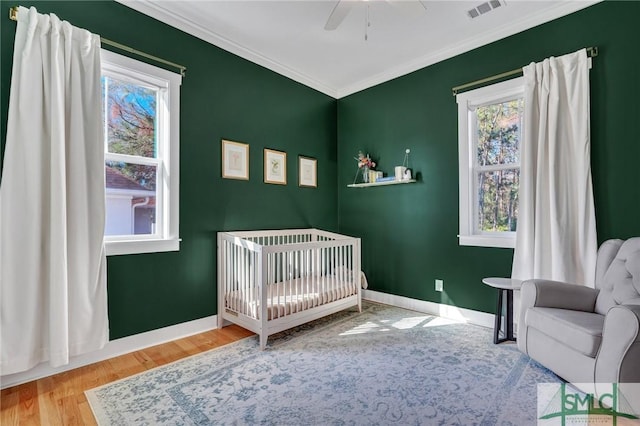 bedroom with crown molding, ceiling fan, wood-type flooring, and a crib