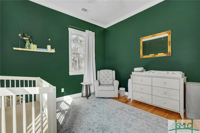 bedroom with a nursery area, crown molding, and light hardwood / wood-style flooring