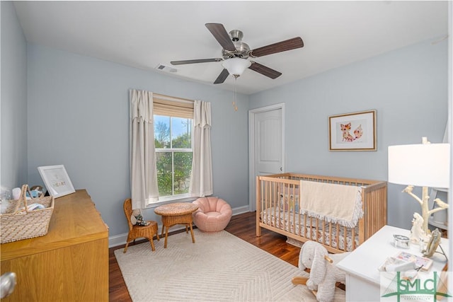 bedroom with ceiling fan, dark hardwood / wood-style flooring, and a crib