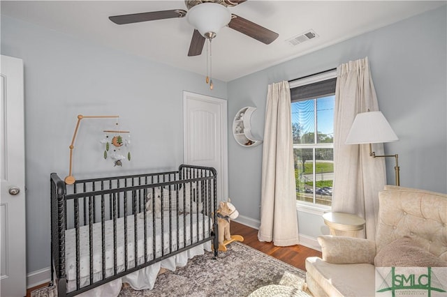 bedroom featuring hardwood / wood-style flooring, a nursery area, and ceiling fan