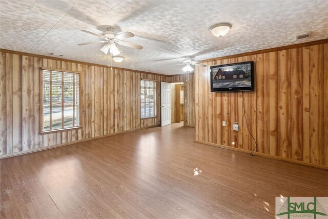 unfurnished living room with hardwood / wood-style flooring, ceiling fan, crown molding, and wooden walls