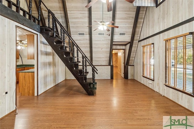 foyer with ceiling fan, wood-type flooring, high vaulted ceiling, and wood walls