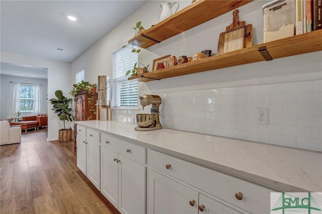 kitchen with tasteful backsplash, light stone countertops, white cabinets, and light wood-type flooring