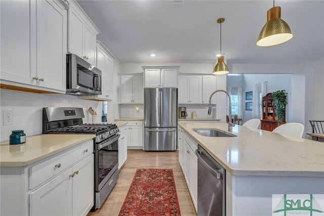 kitchen featuring white cabinetry, sink, hanging light fixtures, a center island with sink, and appliances with stainless steel finishes