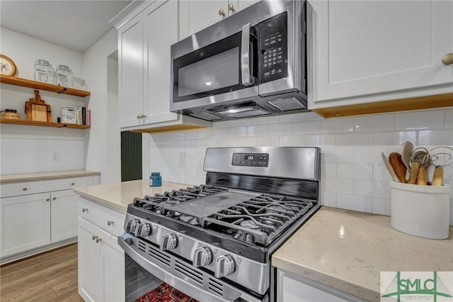 kitchen with light stone countertops, appliances with stainless steel finishes, backsplash, wood-type flooring, and white cabinetry