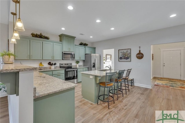 kitchen featuring light hardwood / wood-style flooring, light stone countertops, appliances with stainless steel finishes, decorative light fixtures, and a breakfast bar area