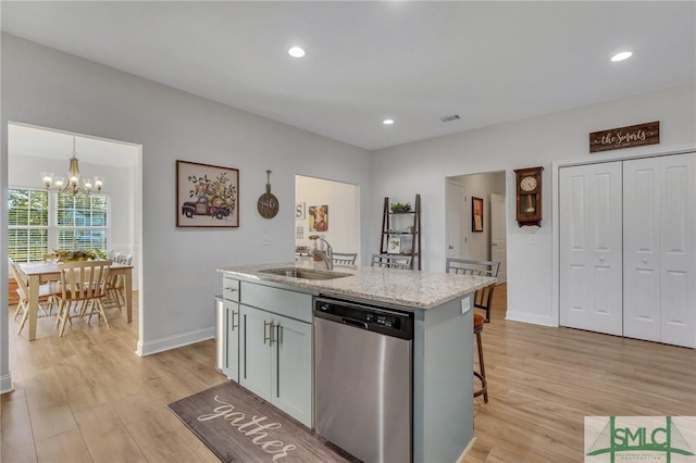 kitchen with light stone countertops, stainless steel dishwasher, sink, a notable chandelier, and an island with sink