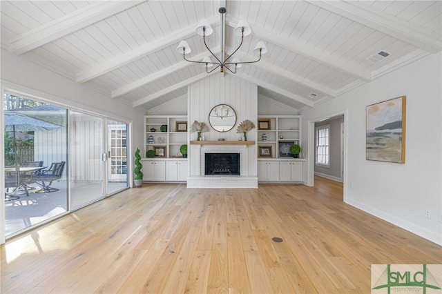 unfurnished living room featuring vaulted ceiling with beams, built in shelves, light wood-type flooring, a fireplace, and a chandelier