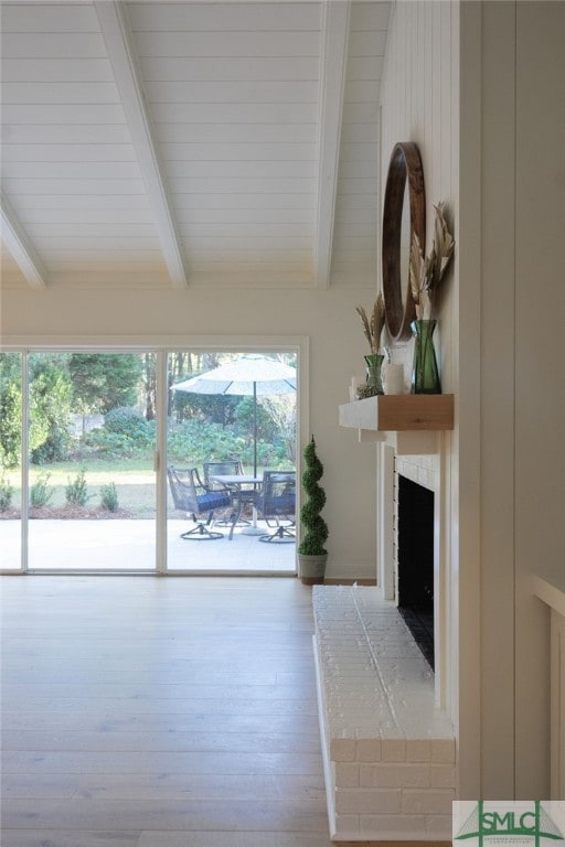 unfurnished living room featuring beam ceiling, wood-type flooring, and a brick fireplace