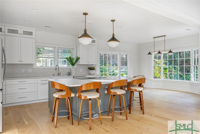 kitchen featuring pendant lighting, backsplash, light hardwood / wood-style floors, a kitchen island, and white cabinetry