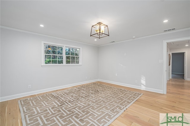 spare room with wood-type flooring, crown molding, and an inviting chandelier