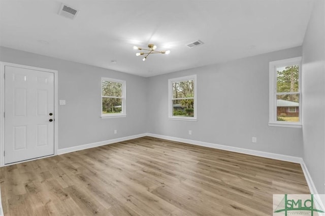 unfurnished room with an inviting chandelier, a wealth of natural light, and light hardwood / wood-style floors