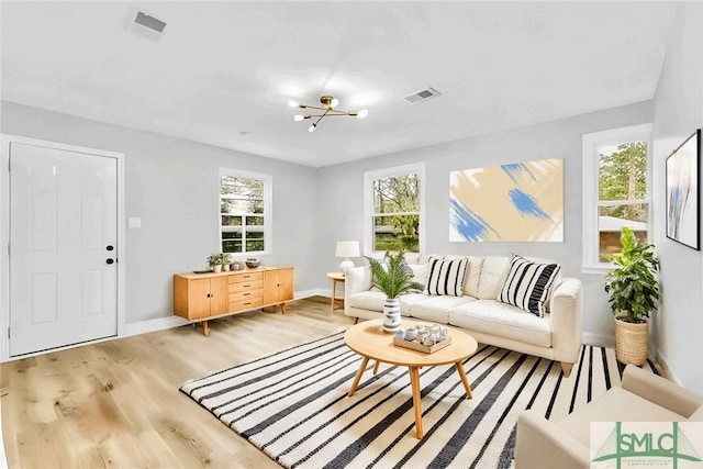 living room featuring a healthy amount of sunlight, a chandelier, and light wood-type flooring