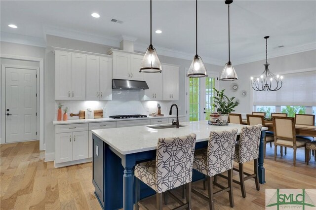 kitchen featuring white cabinetry, sink, decorative light fixtures, a center island with sink, and exhaust hood