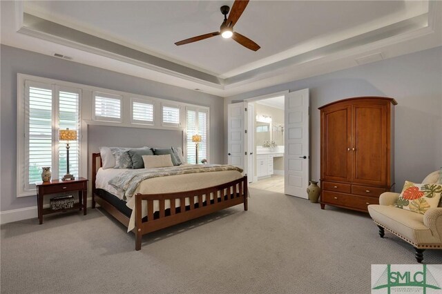 bedroom with a tray ceiling, ensuite bath, ceiling fan, and light colored carpet