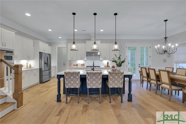 kitchen with a breakfast bar, stainless steel appliances, a kitchen island with sink, decorative light fixtures, and white cabinets