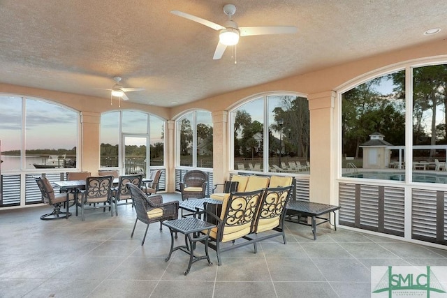 sunroom featuring ceiling fan and a water view