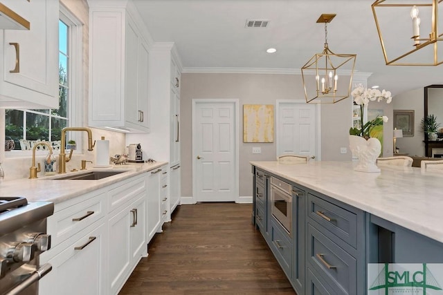 kitchen with light stone counters, built in microwave, sink, white cabinets, and hanging light fixtures