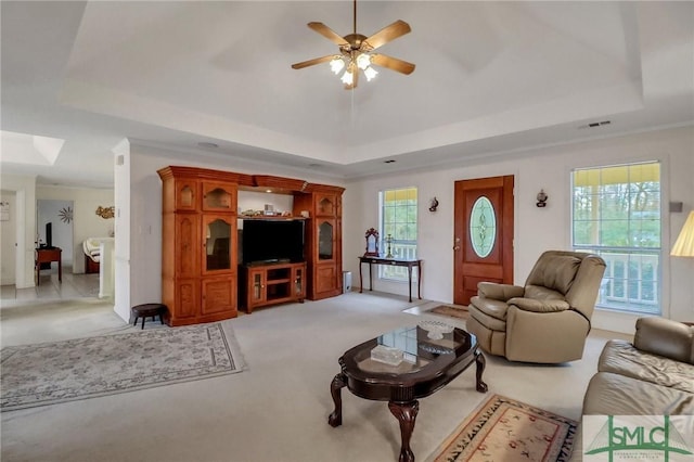 living room with ceiling fan, light colored carpet, ornamental molding, and a tray ceiling