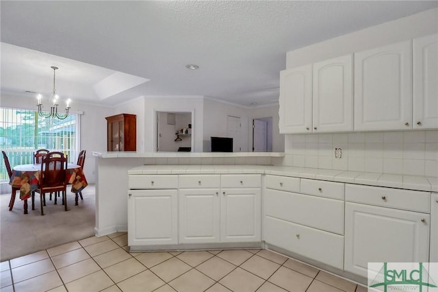 kitchen with white cabinetry, hanging light fixtures, a notable chandelier, light tile patterned floors, and ornamental molding