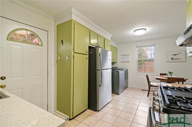 kitchen with washing machine and dryer, green cabinets, crown molding, light tile patterned floors, and appliances with stainless steel finishes