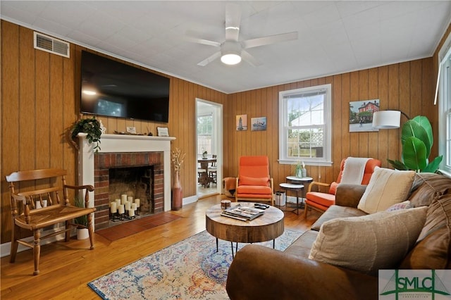 living room with ceiling fan, light hardwood / wood-style flooring, wood walls, and a brick fireplace