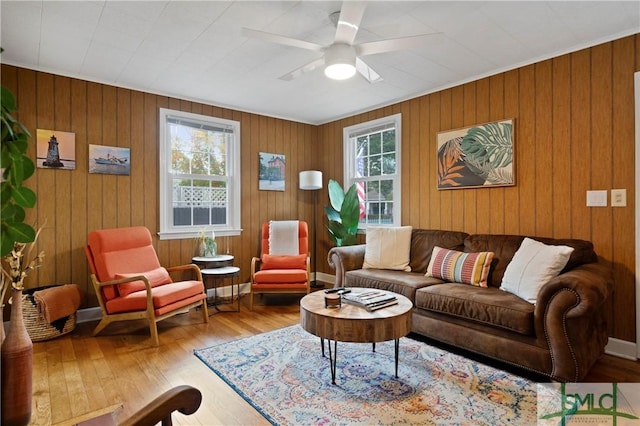 living room with light hardwood / wood-style flooring, ceiling fan, and wood walls