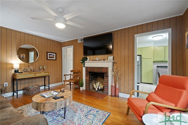 living room featuring ceiling fan, washer / clothes dryer, hardwood / wood-style floors, a fireplace, and ornamental molding