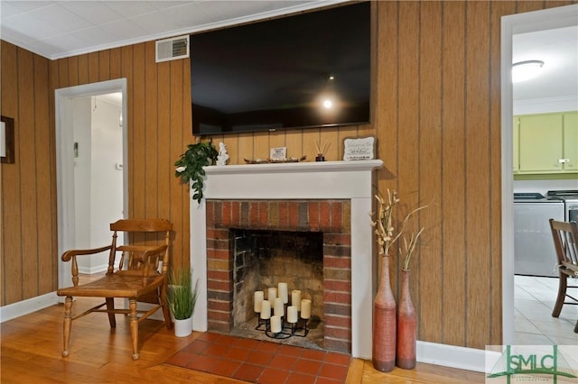 living area featuring washer and dryer, wood walls, crown molding, and a fireplace