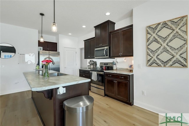 kitchen featuring a kitchen breakfast bar, sink, hanging light fixtures, appliances with stainless steel finishes, and light hardwood / wood-style floors