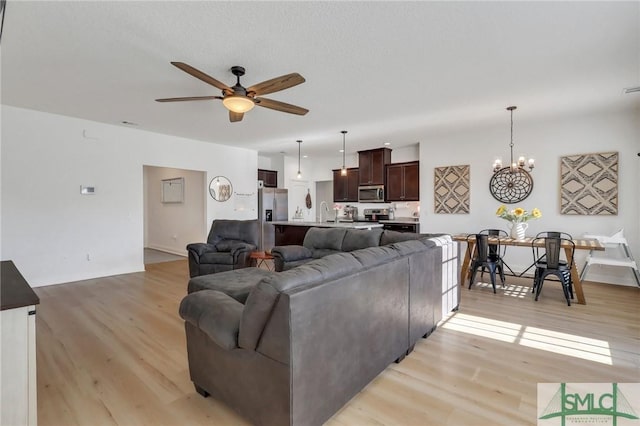 living room featuring a textured ceiling, ceiling fan with notable chandelier, light hardwood / wood-style floors, and sink